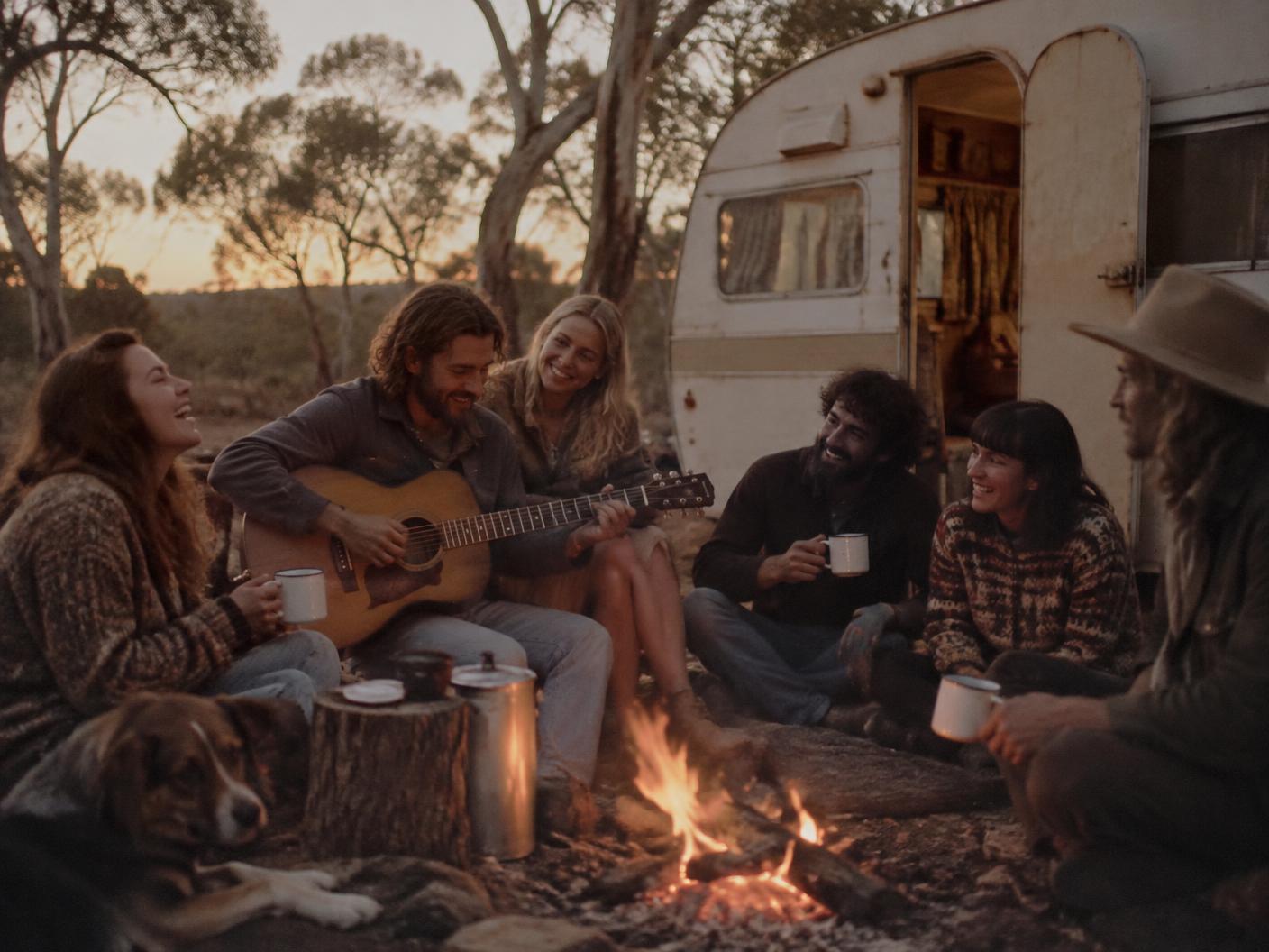 Friends sharing tea and music around a campfire